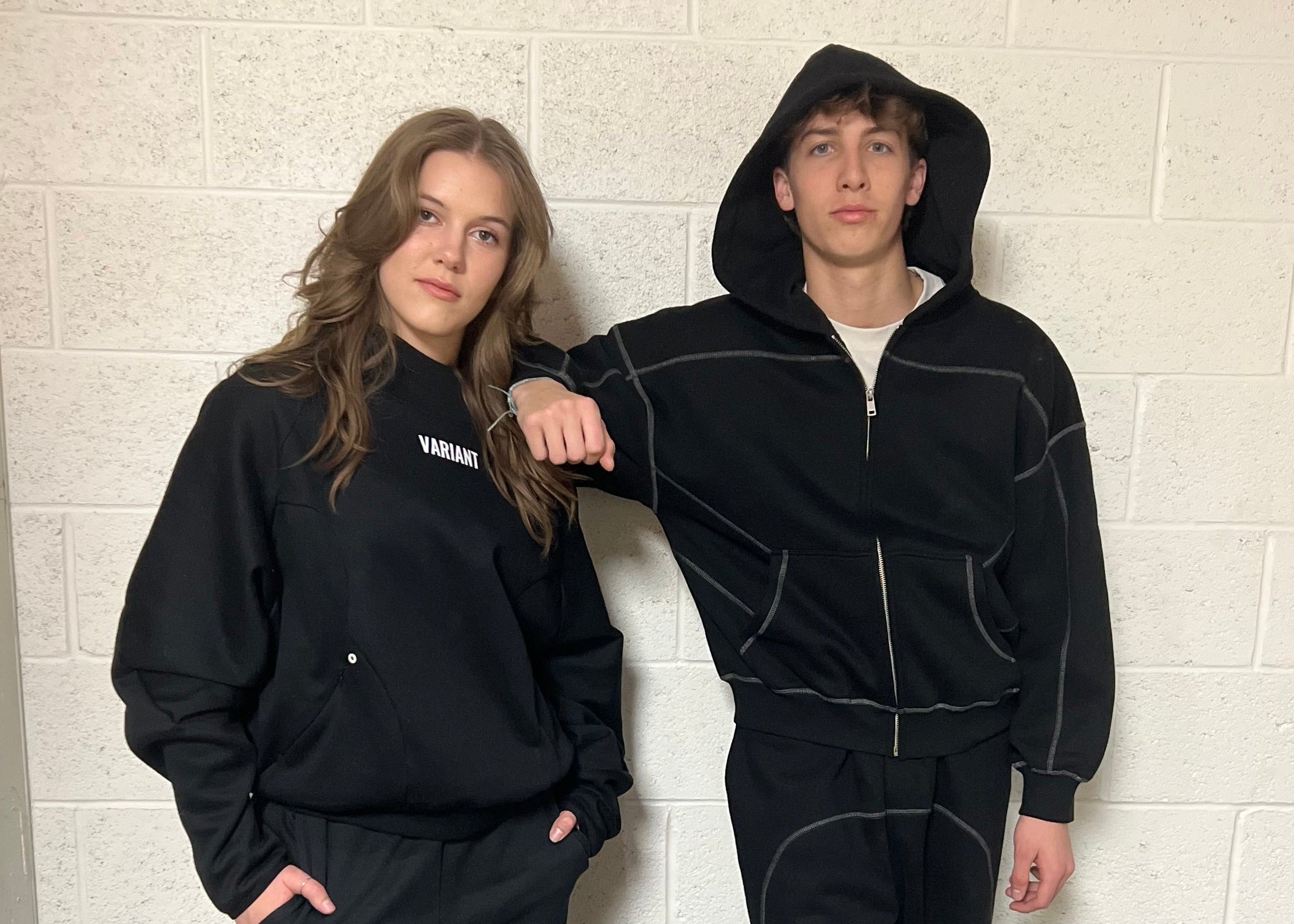 Two people wearing black tracksuits with 'Variant' branding against a white tiled wall.